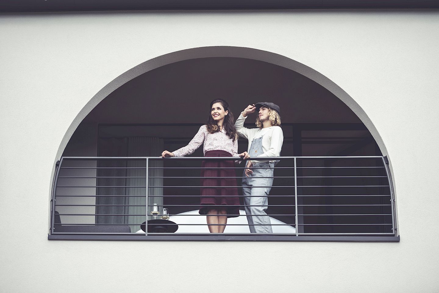 Two people on an elegant balcony, smiling and looking into the distance.