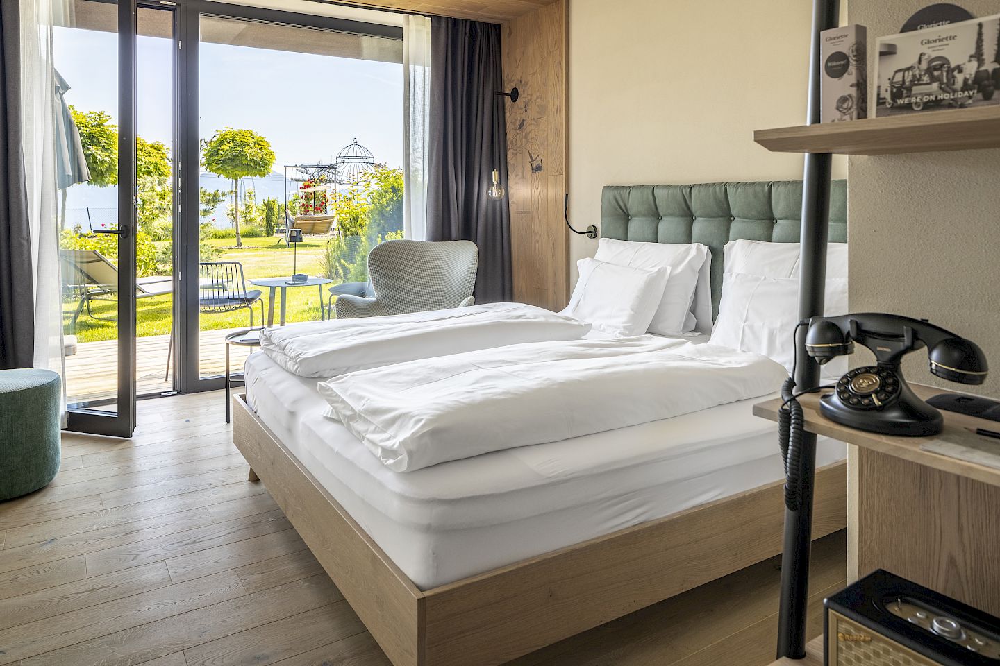 Cozy hotel room with double bed, lake view through glass wall. Wooden floor, antique phone on shelf.