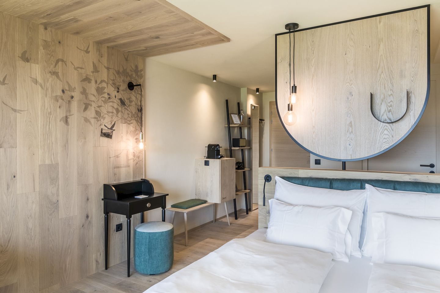 Modern hotel room with wooden elements, stylish lighting, and a small desk with a stool.