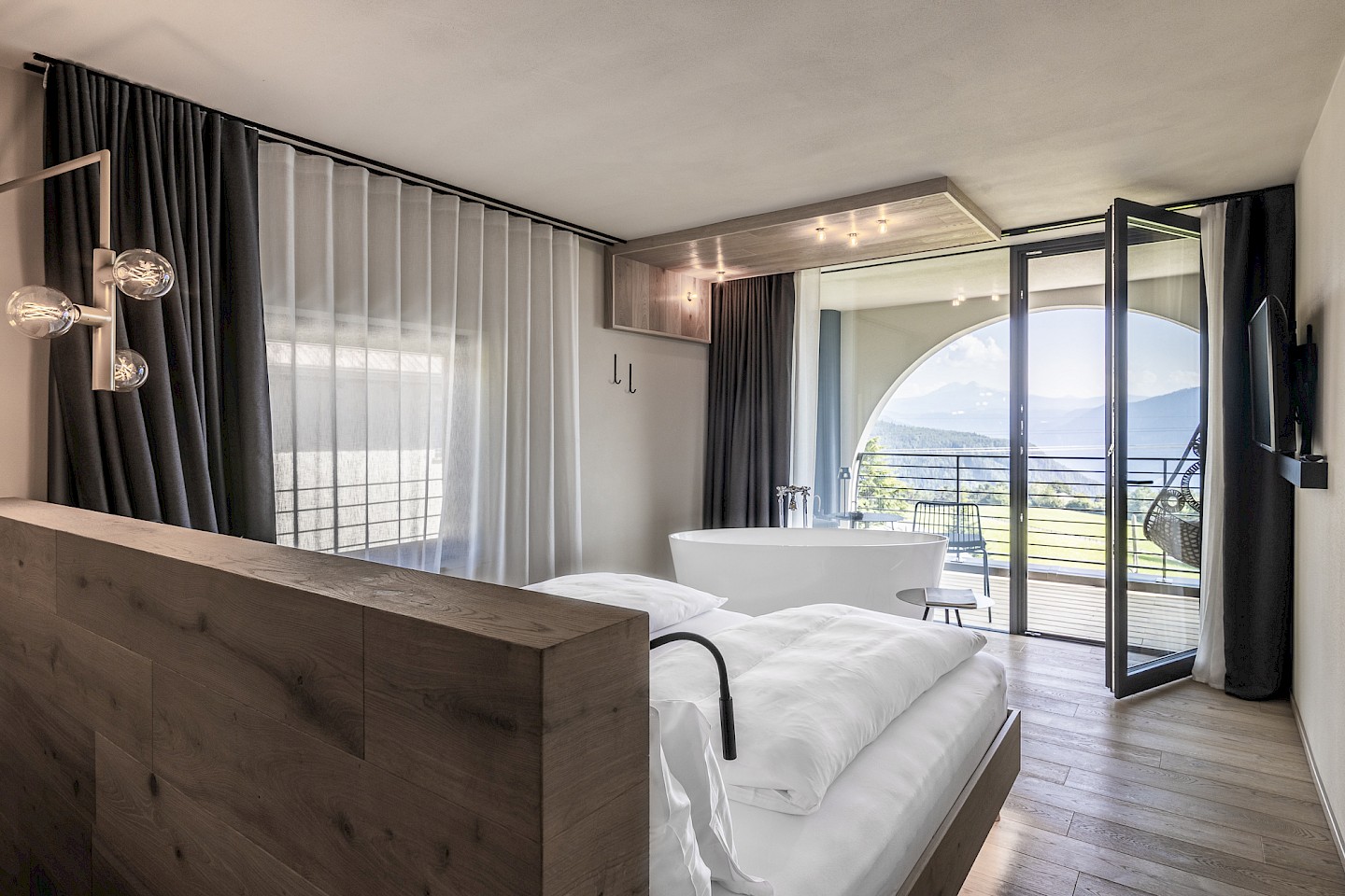 Lorenzi Suite des Gloriette Guesthouse mit Bett, freistehender Badewanne und großem Fenster mit Blick auf Berge und See.
