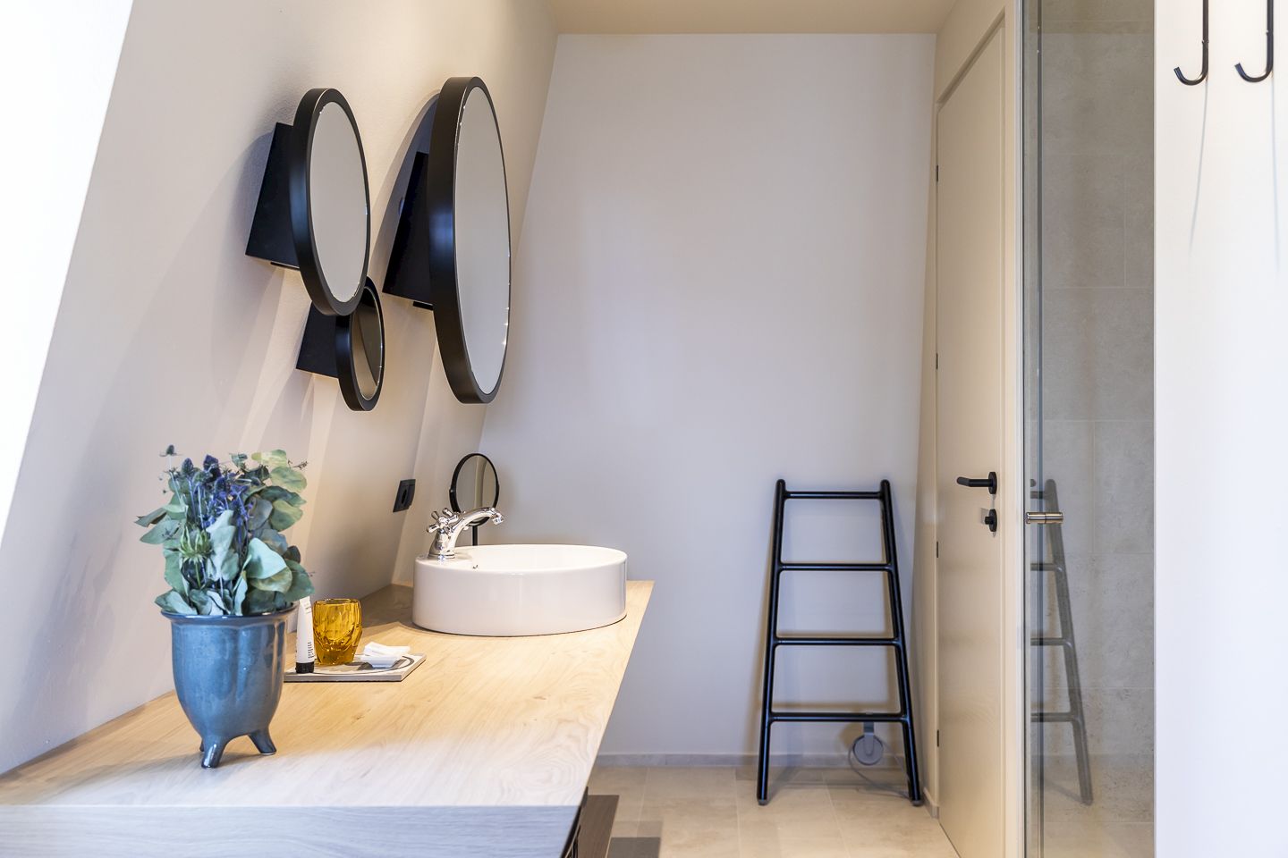 Il bagno del Lorenzi Suite con lavandino rotondo, bancone in legno, due specchi e scala, pianta decorativa a sinistra.