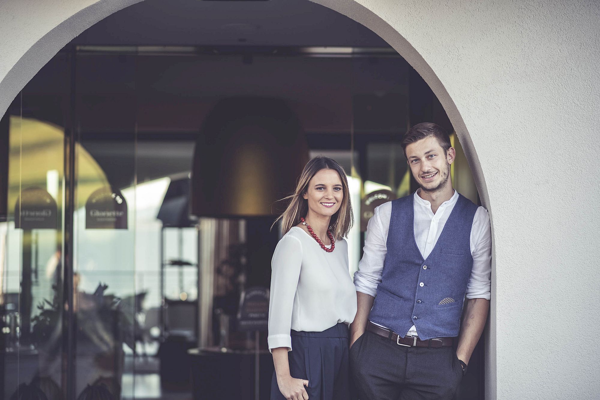 The hosts stand smiling in the entrance area of the Gloriette Guesthouse under an archway.