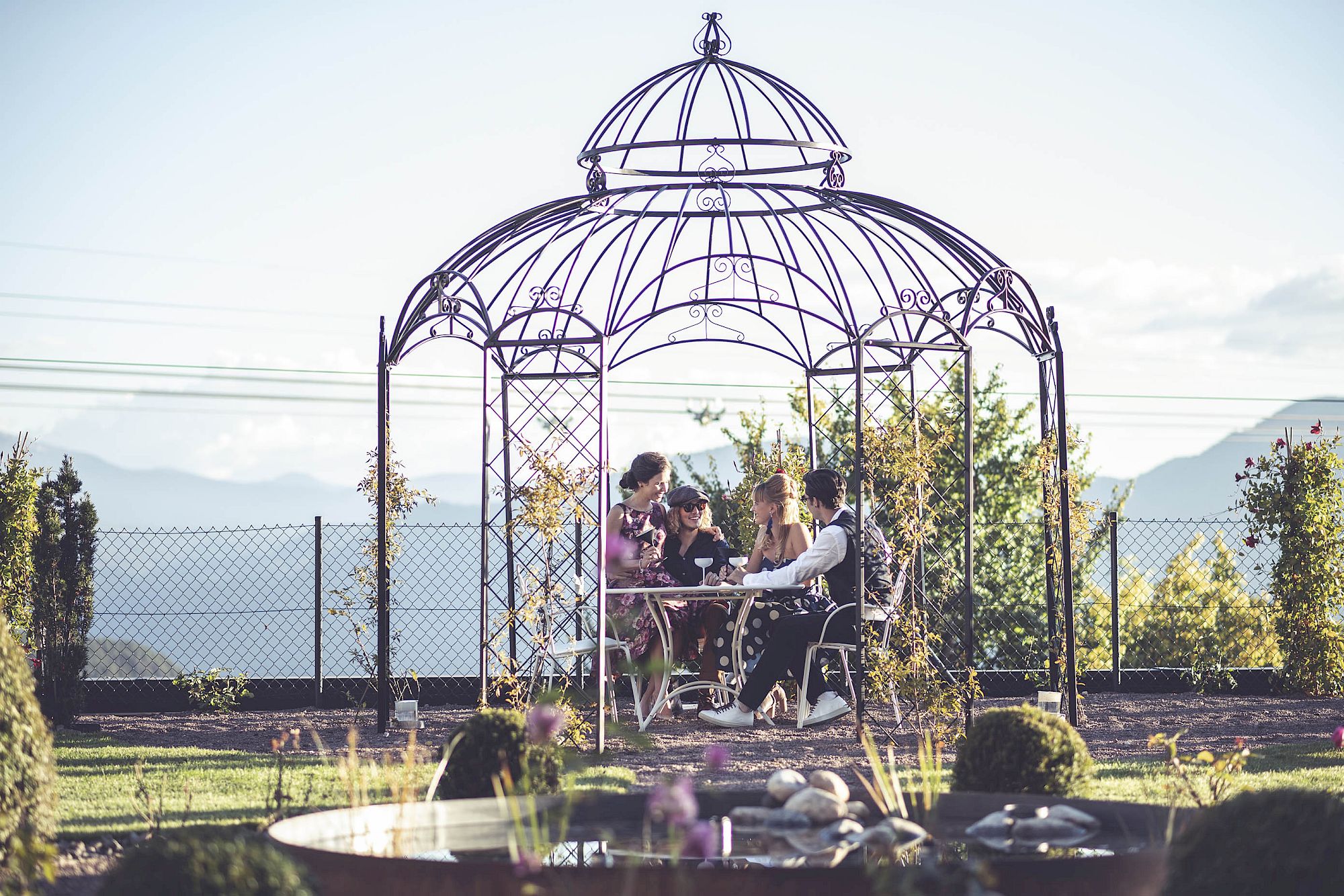Garden gazebo with mountain view. A group of people at a table is having a conversation.
