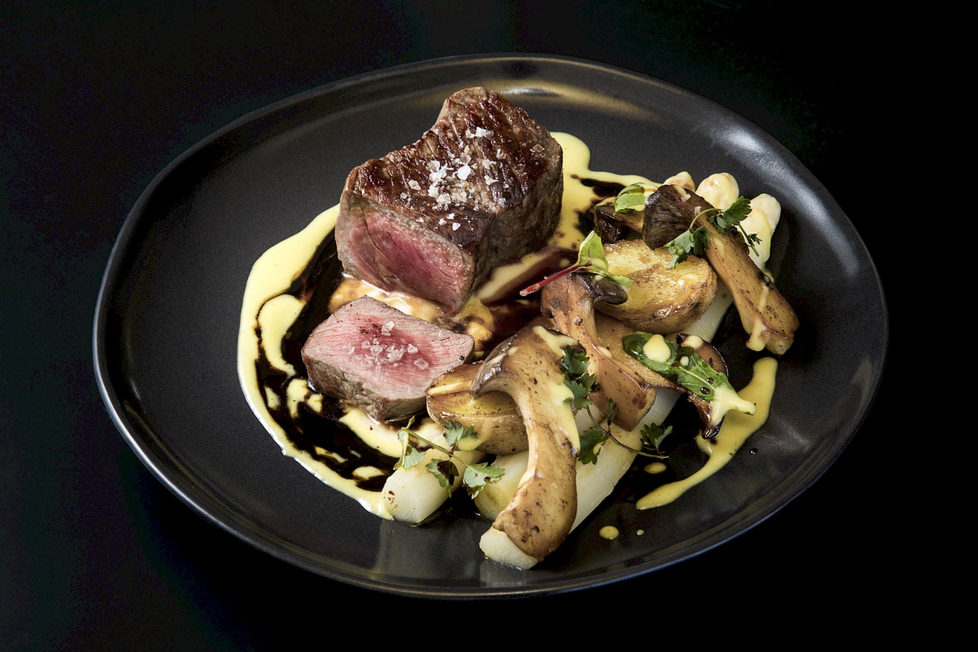 Ein zartes Rinderfilet auf einem Teller, serviert mit Spargel, Pilzen und cremiger Sauce.