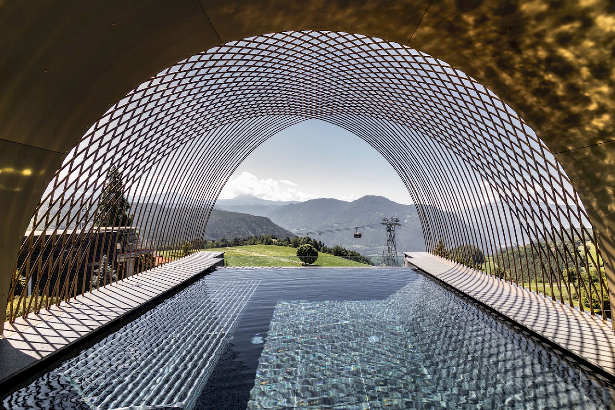 A modern net structure overlooks a the Gloriette Guesthouse infinity pool and a distant mountain landscape.
