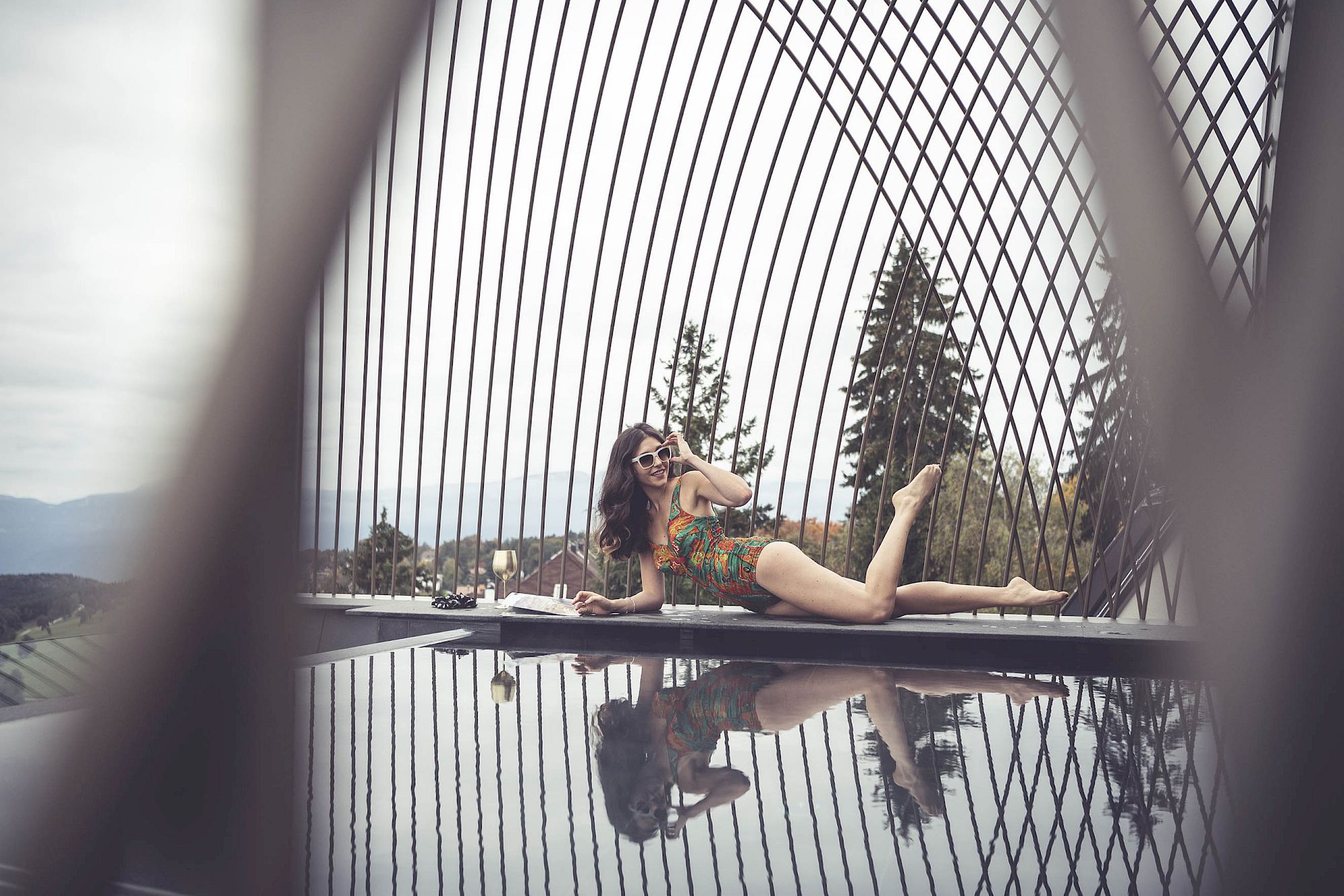 Woman in colorful clothing stylishly lying at the infinity pool with geometric design, surrounded by nature.