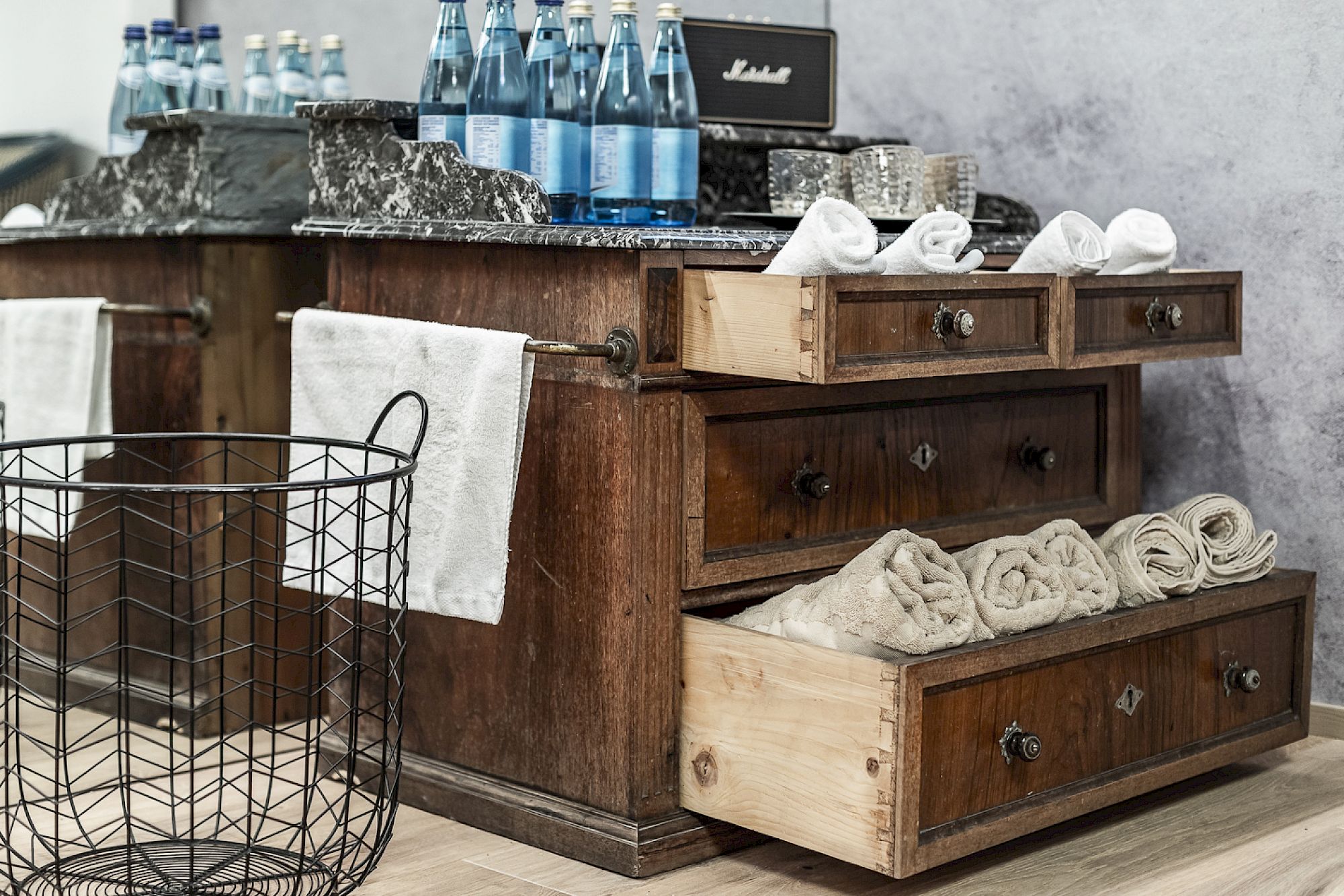 Rustic wooden dresser, towels, water bottles, and a wire basket.