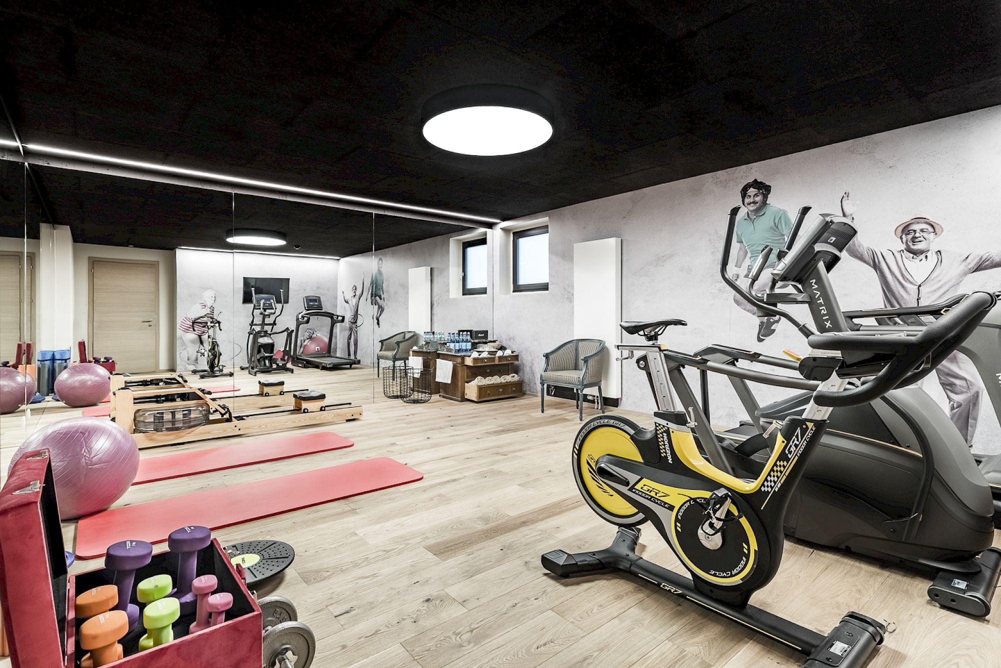 Fitnessstudio mit Hanteln, Yoga-Matten, einem Heimtrainer und modernen Wandzeichnungen. Heller, offener Raum.