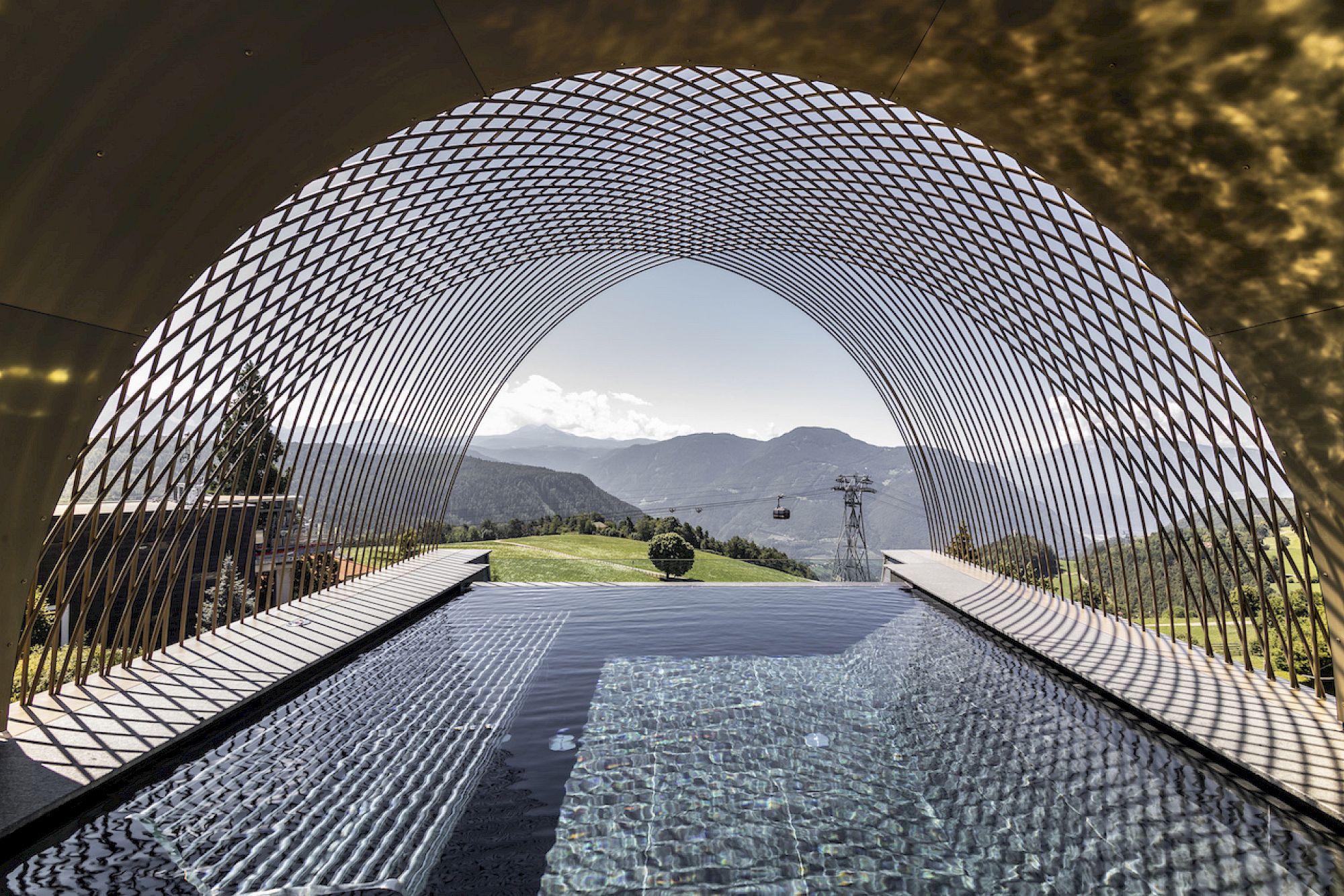 Una moderna struttura a rete sovrasta la infinity pool del Gloriette Guesthouse e un paesaggio montano lontano.