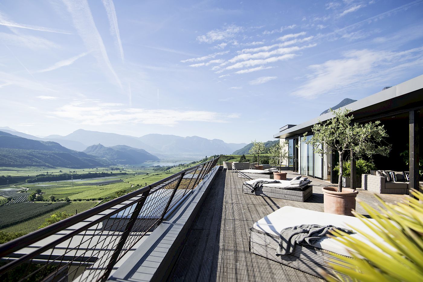 Terrazza del Gius a Caldaro con vista su una vasta valle e montagne sotto il cielo blu. Lettini e piante.