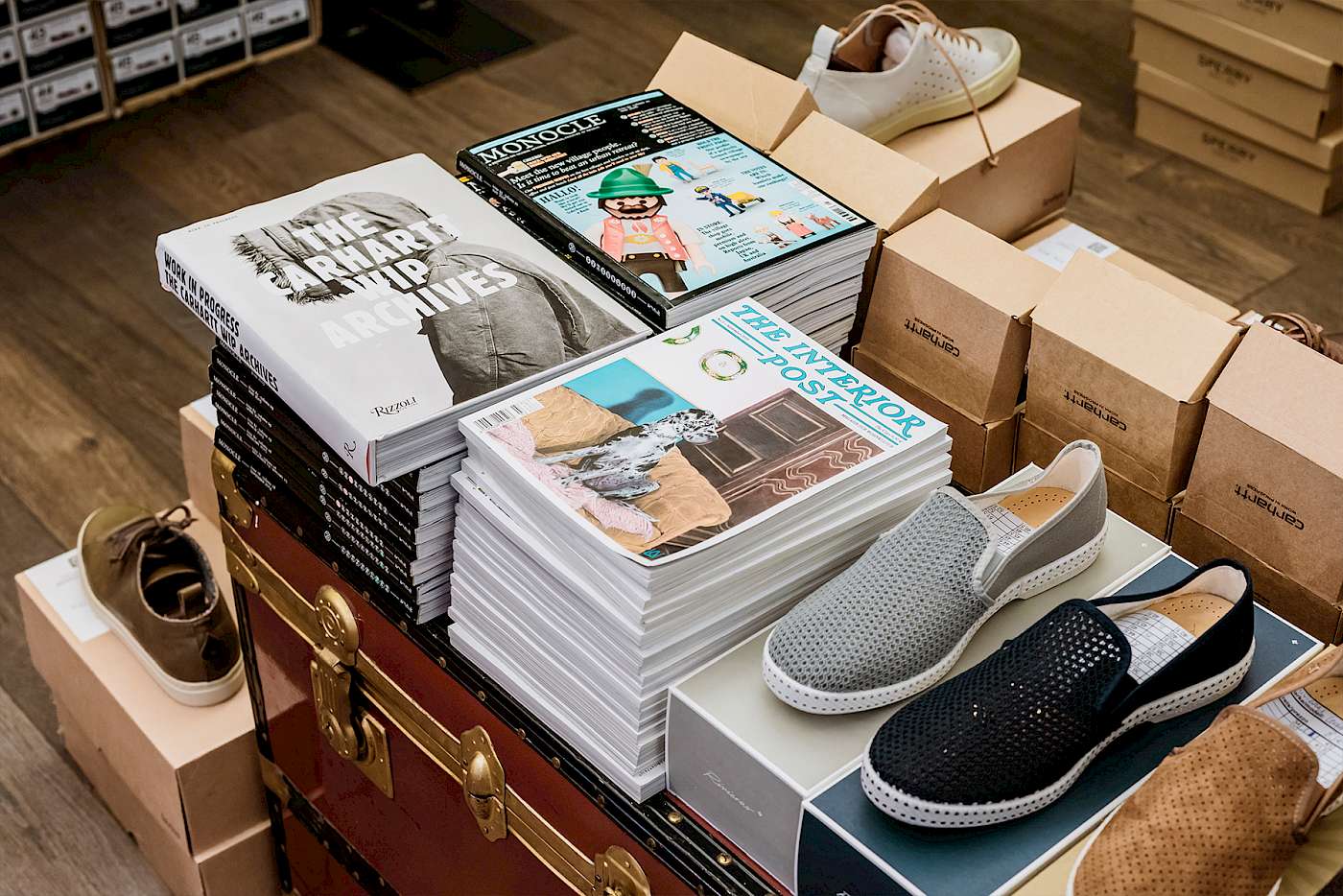 Stapel von Büchern und Zeitschriften neben Schuhen und Kartons in einem Geschäft mit Holzboden.