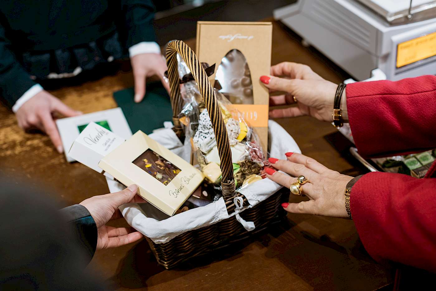 Korb mit Pralinen und Schokoladen, von Händen gehalten, auf Holztisch in Geschäft. QQQQ Cesto con dolci e cioccolatini, tenuto da mani, su tavolo di legno in un negozio. QQQQ Basket with chocolates and sweets, held by hands, on wooden table in a shop.