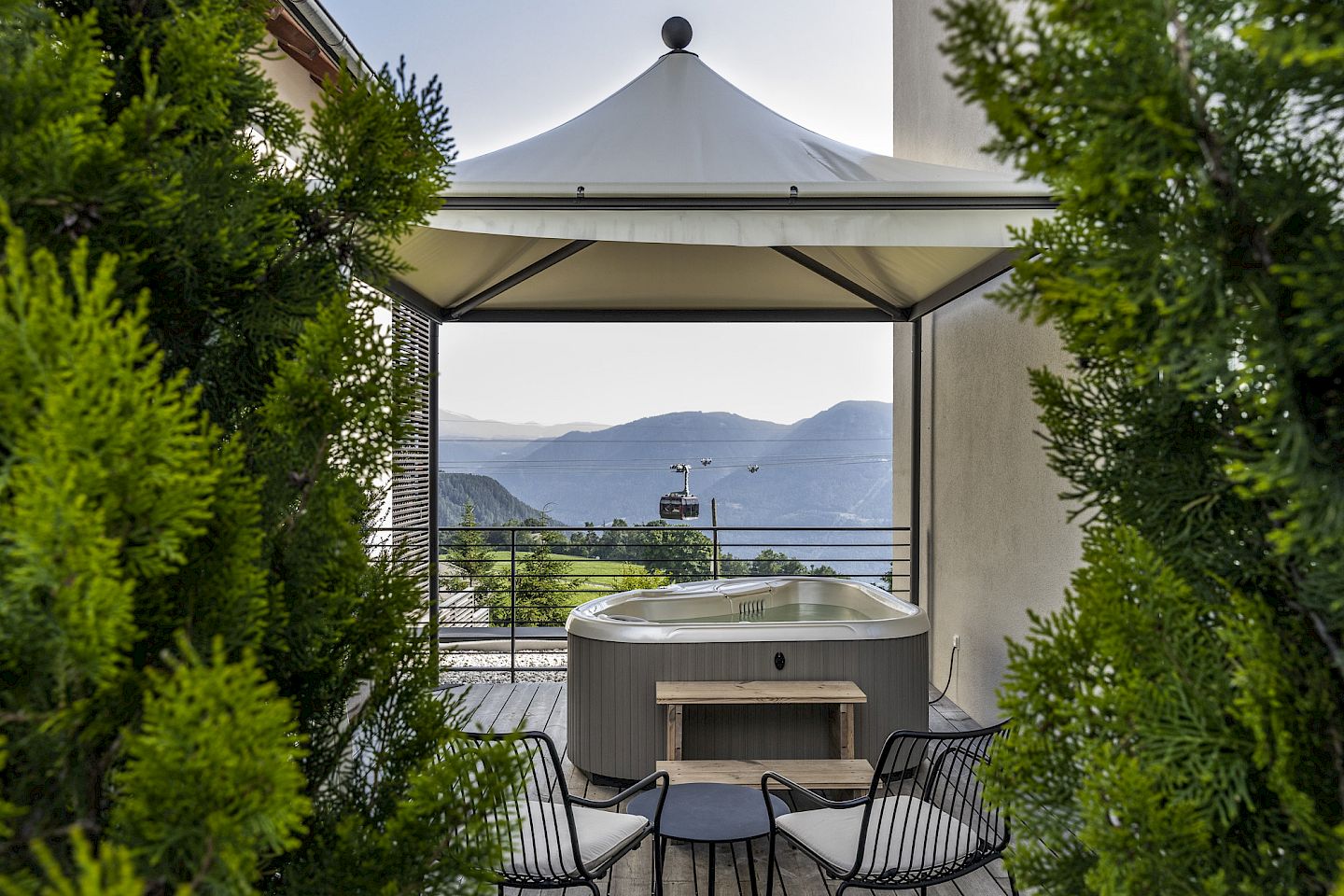 Außenbereich der Terrassen Whirlpool Suite mit Whirlpool unter einem Pavillon, umgeben von Bäumen, mit Blick auf Berge.