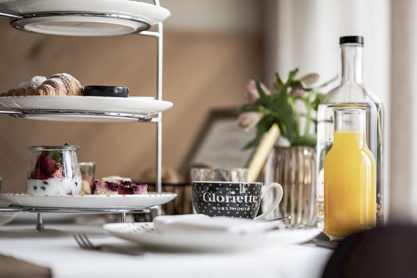 An elegant breakfast table with pastries, fruit salad, coffee cup, orange juice, and a vase of flowers.