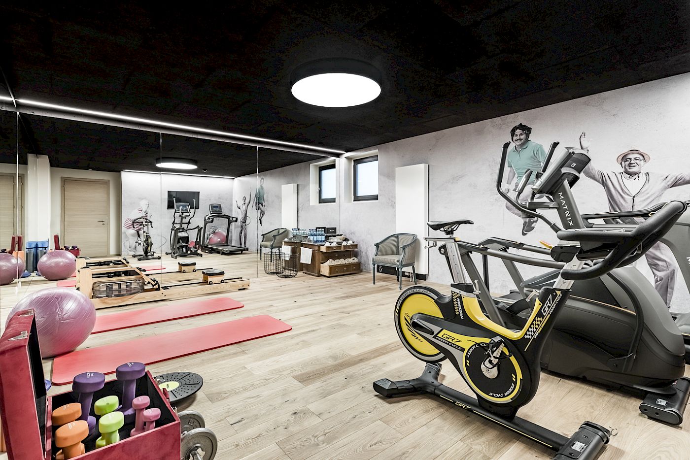 Fitnessstudio mit Hanteln, Yoga-Matten, einem Heimtrainer und modernen Wandzeichnungen. Heller, offener Raum.