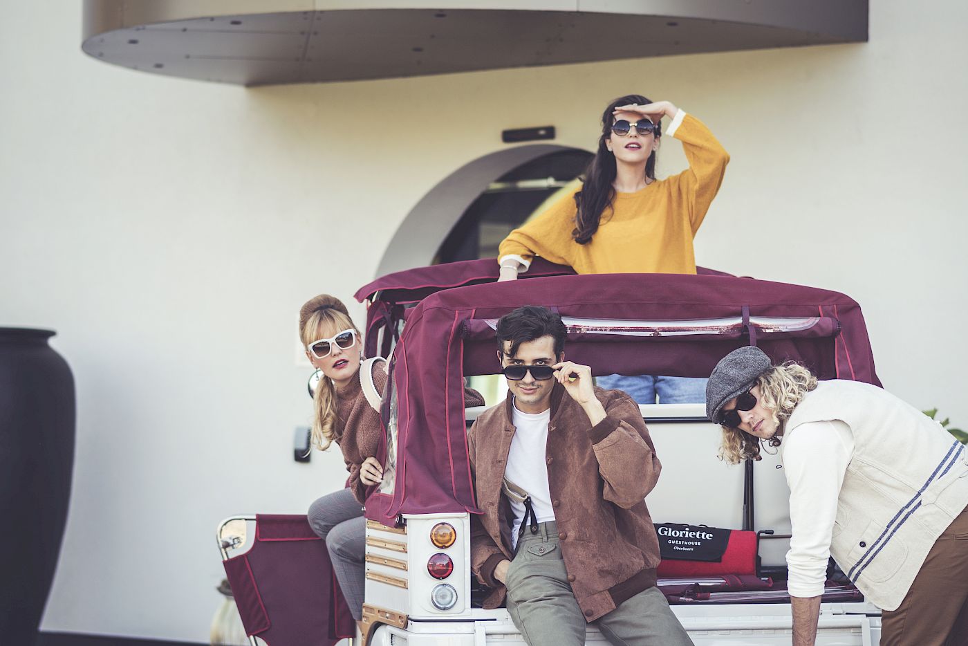 Vier Personen posieren fröhlich auf einem kleinen, weißen Fahrzeug vor einem modernen Gebäude.