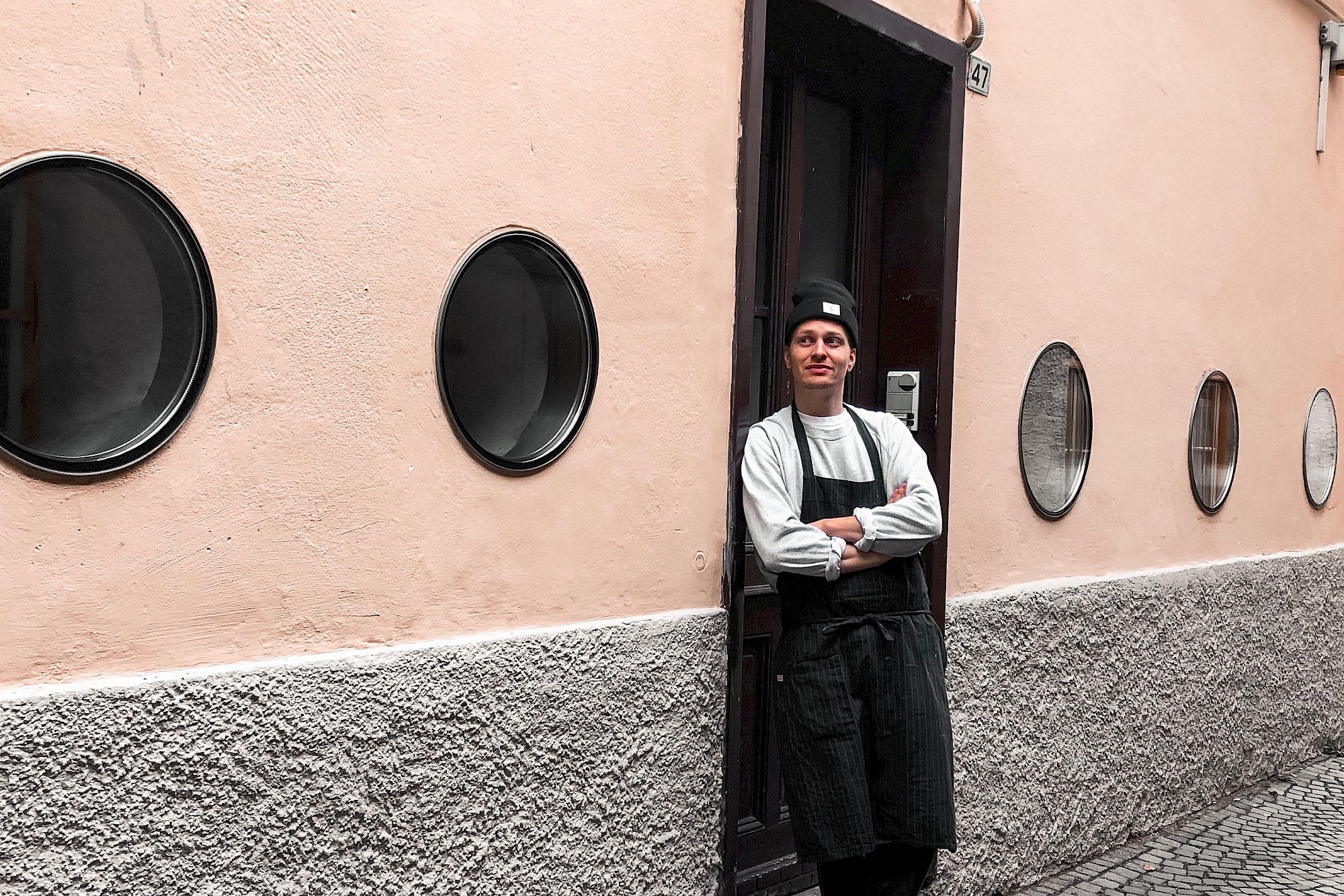 Person leaning against a building wall with "Fifty Eight" sign and round windows.