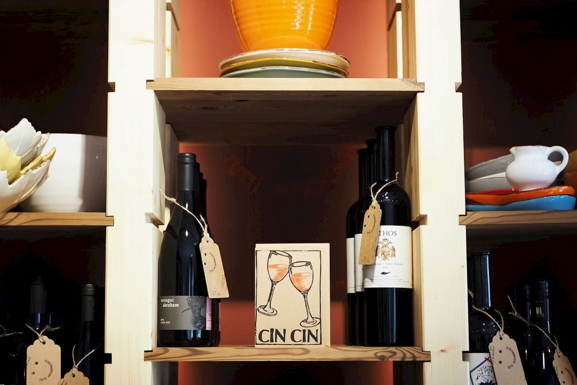 Shelf with wine bottles, ceramic dishes, and a sign saying "Cin Cin" in the center.