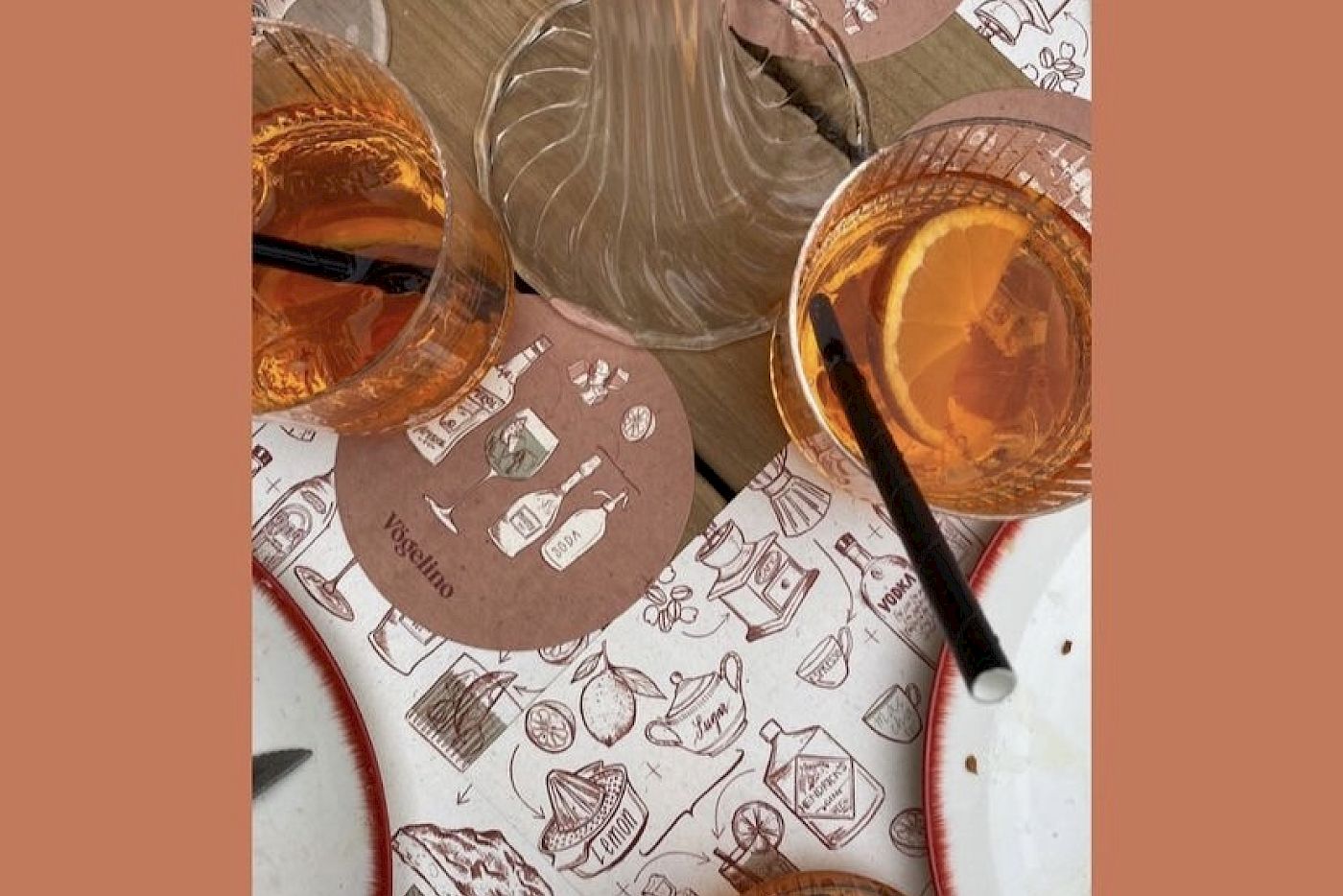 Coasters and glasses with drinks on illustrated table mat. Warm, inviting atmosphere.