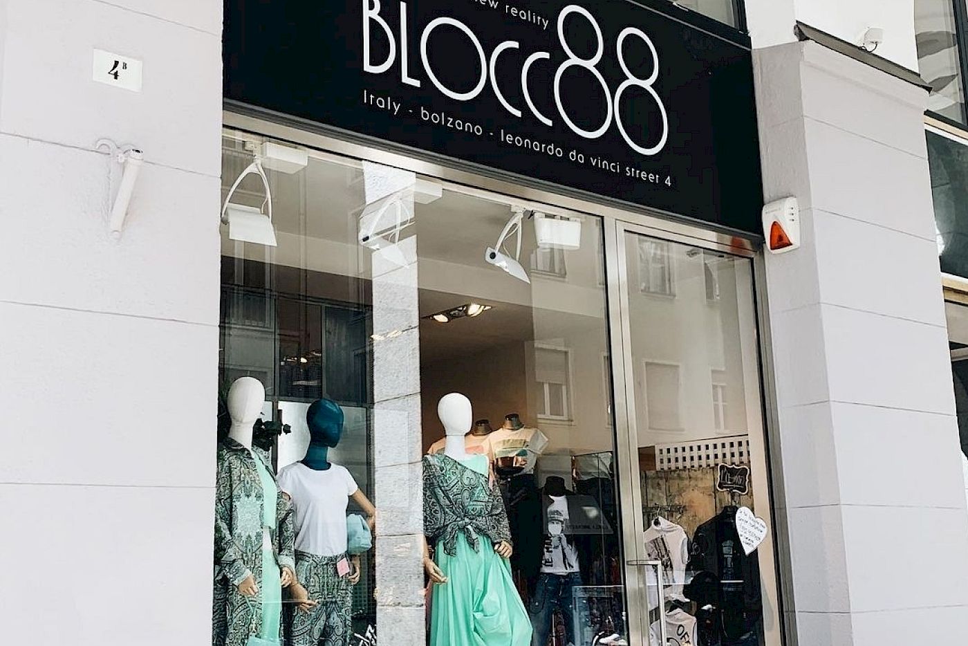 Außenansicht eines Modegeschäfts namens Blocc88 mit eleganten Kleidern im Schaufenster unter Arkaden.