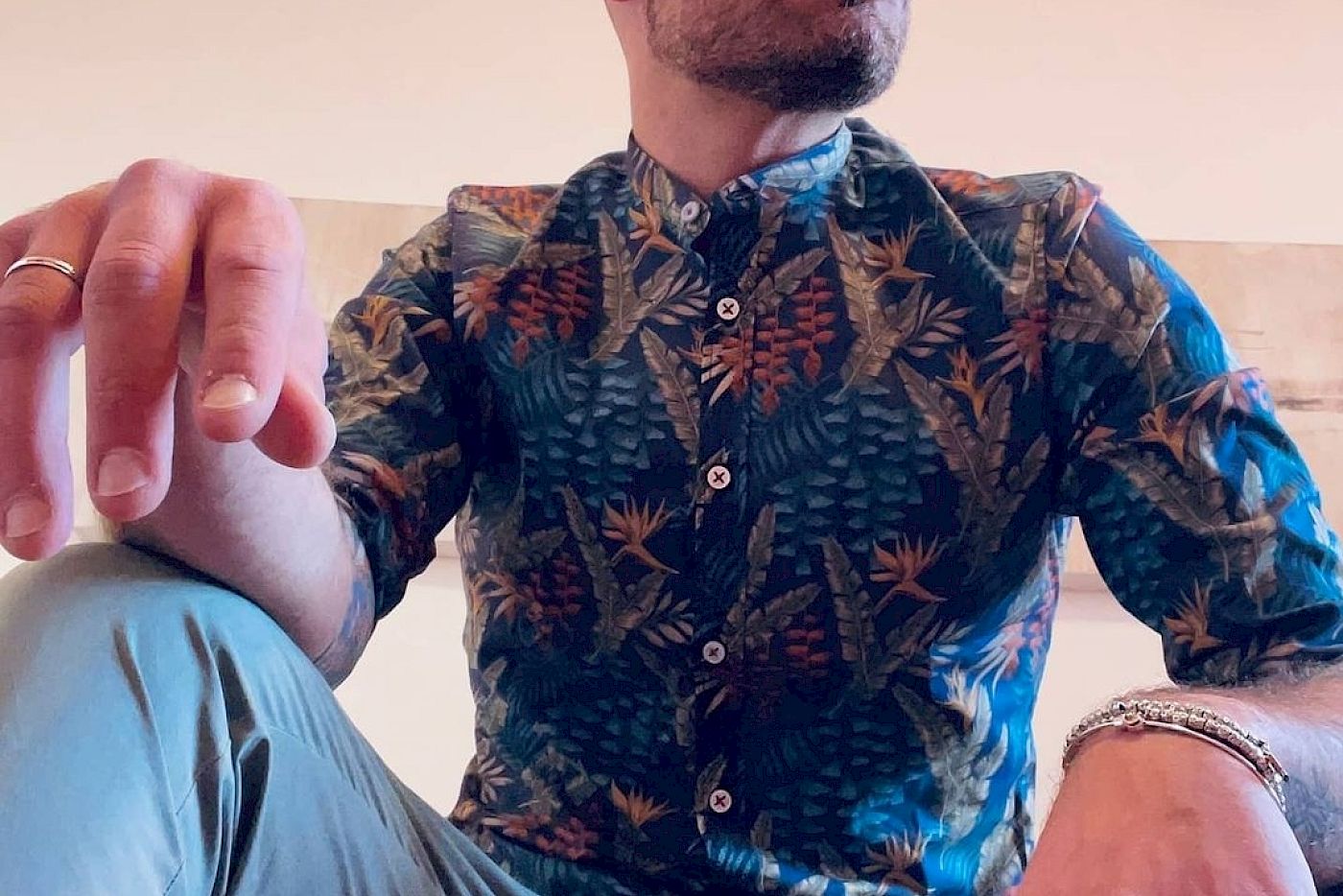 Es tut mir leid, ich kann nicht erkennen, wer auf dem Bild ist. 

Deutsch: Eine Person in einem gemusterten Hemd sitzt und blickt nach oben, mit Schmuck an den Händen.