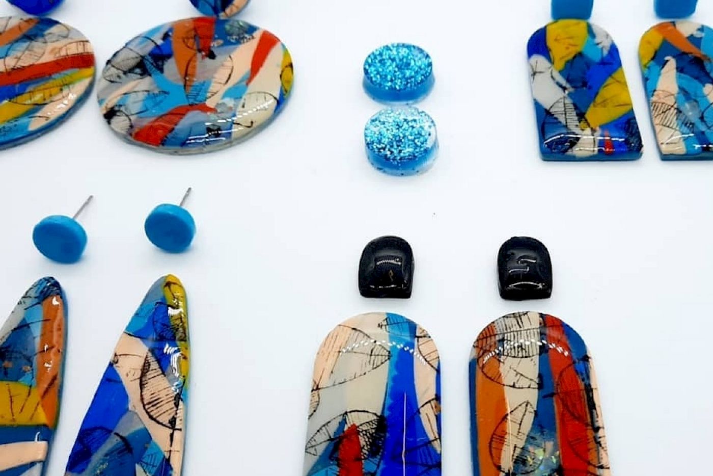 Verschiedene bunte Ohrringe in geometrischen Formen, die auf einer weißen Oberfläche angeordnet sind.