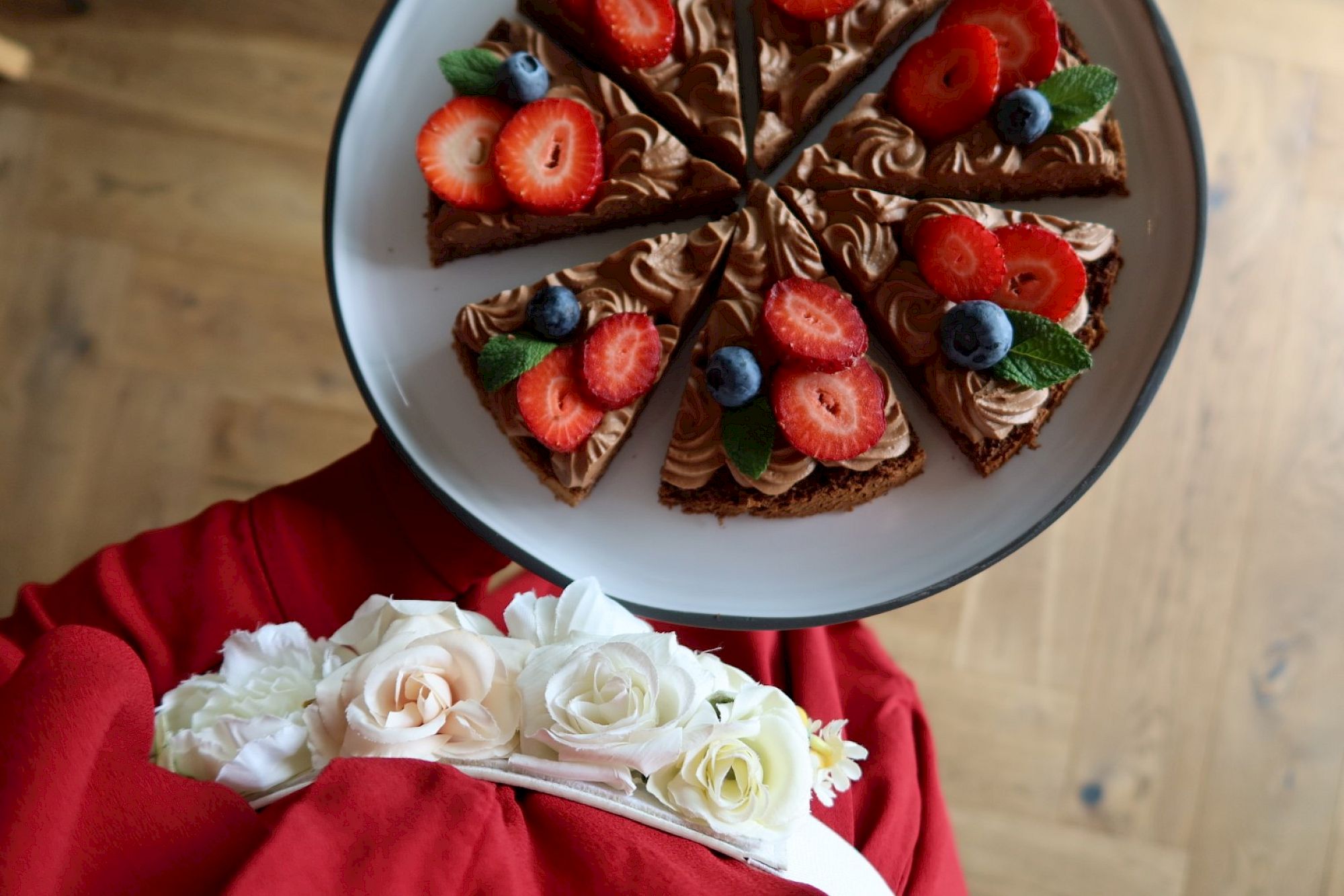 Un piatto di torta al cioccolato guarnita con fragole, mirtilli e foglie di menta su un vestito rosso.