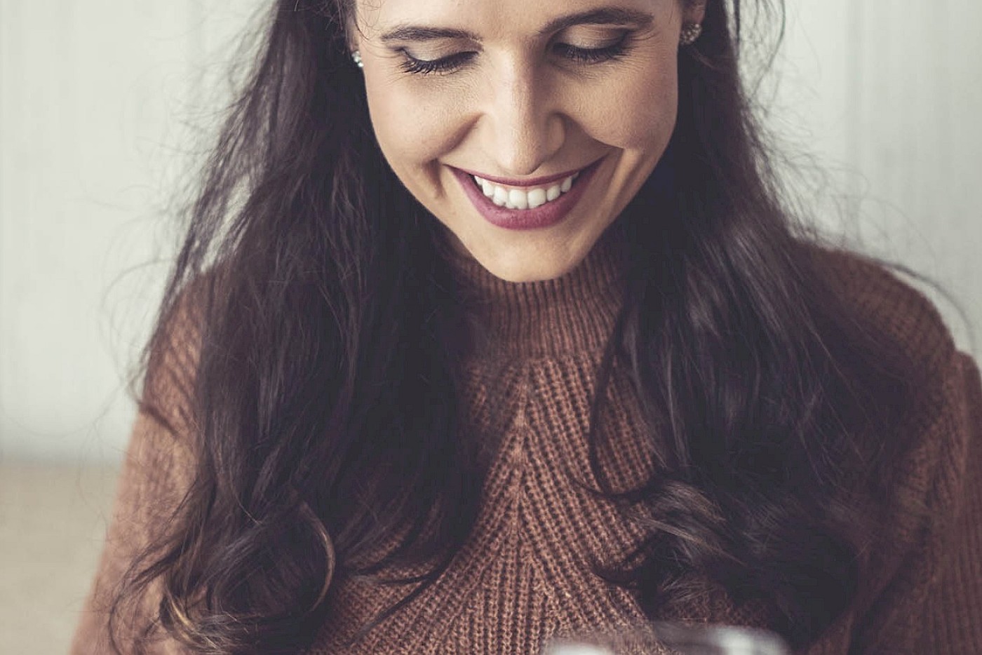 A smiling woman dining at a table, a wine glass in front of her.