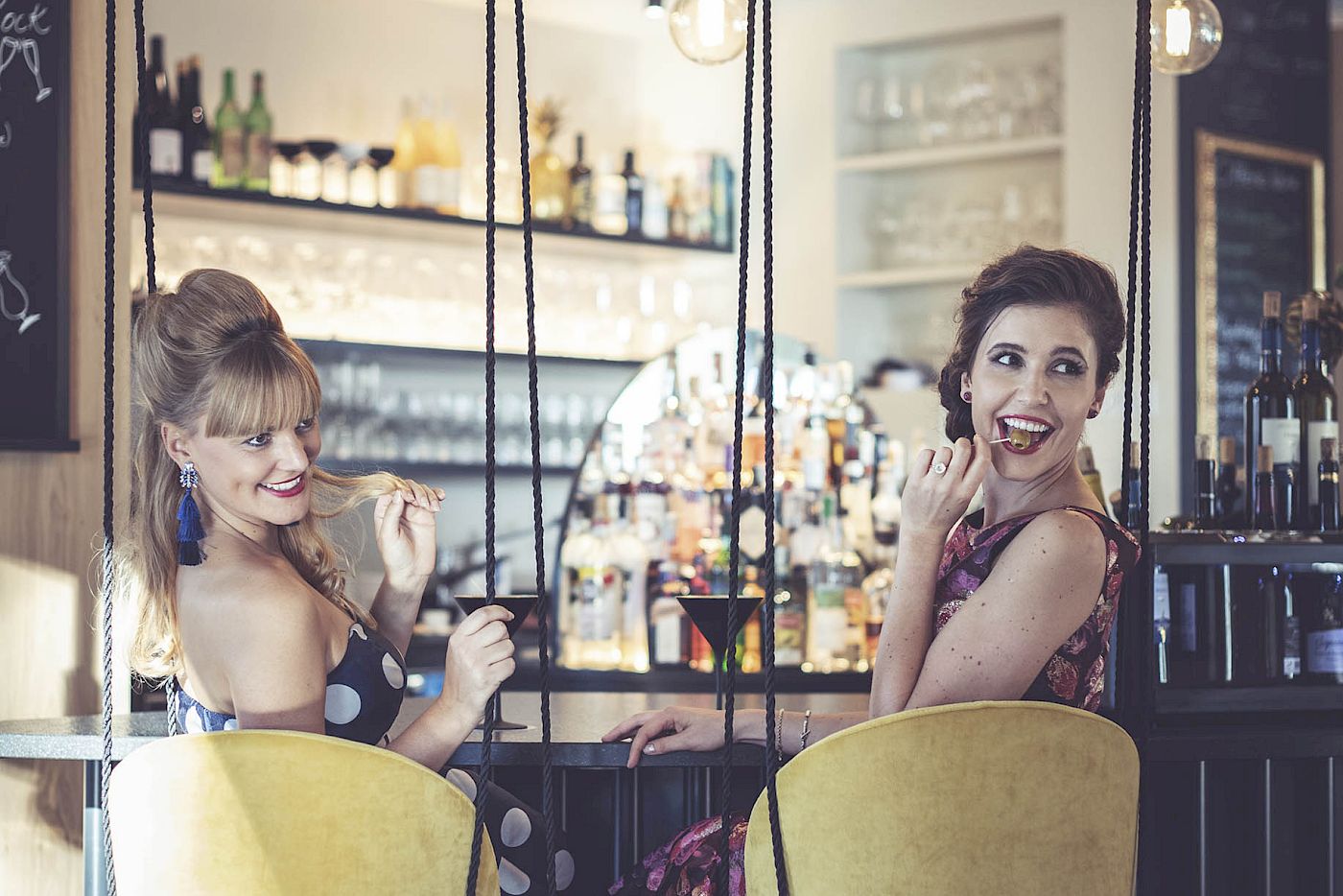 Two women on swings chatting in the stylish bar of Gloriette Guesthouse.